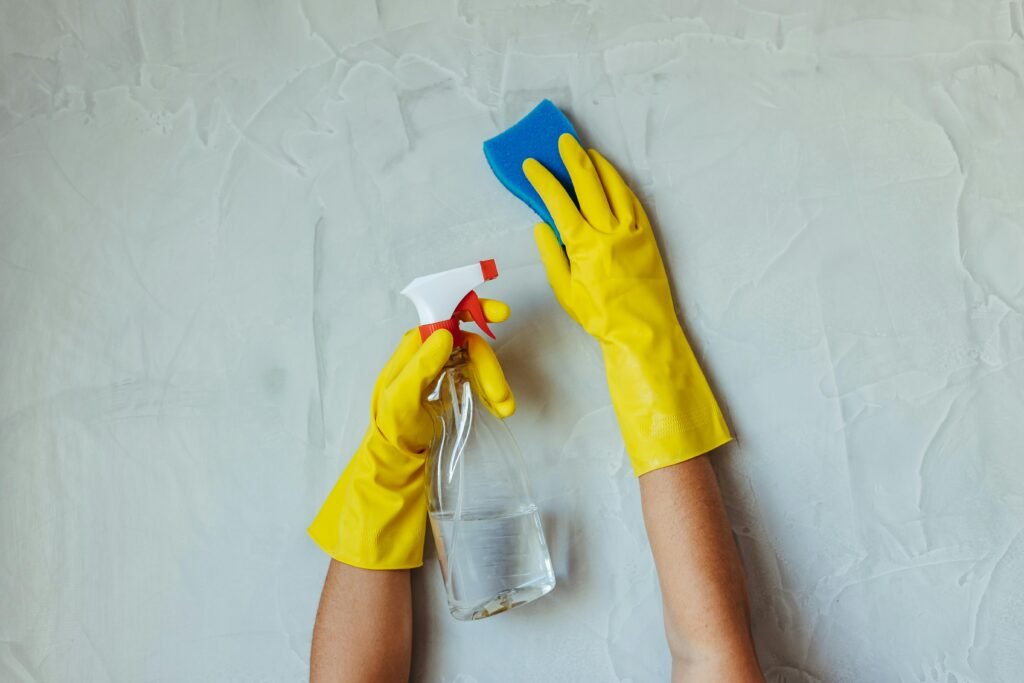 pexels-photo-28576631-28576631 Close-up of hands in yellow gloves cleaning a wall with a spray bottle and sponge.